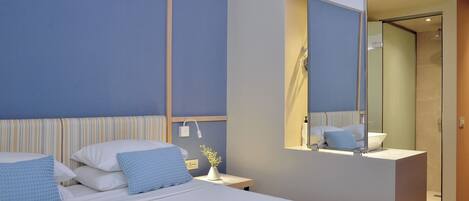 A modern hotel room with a large bed, a bedside table with a lamp, a mirror, and a shower area.