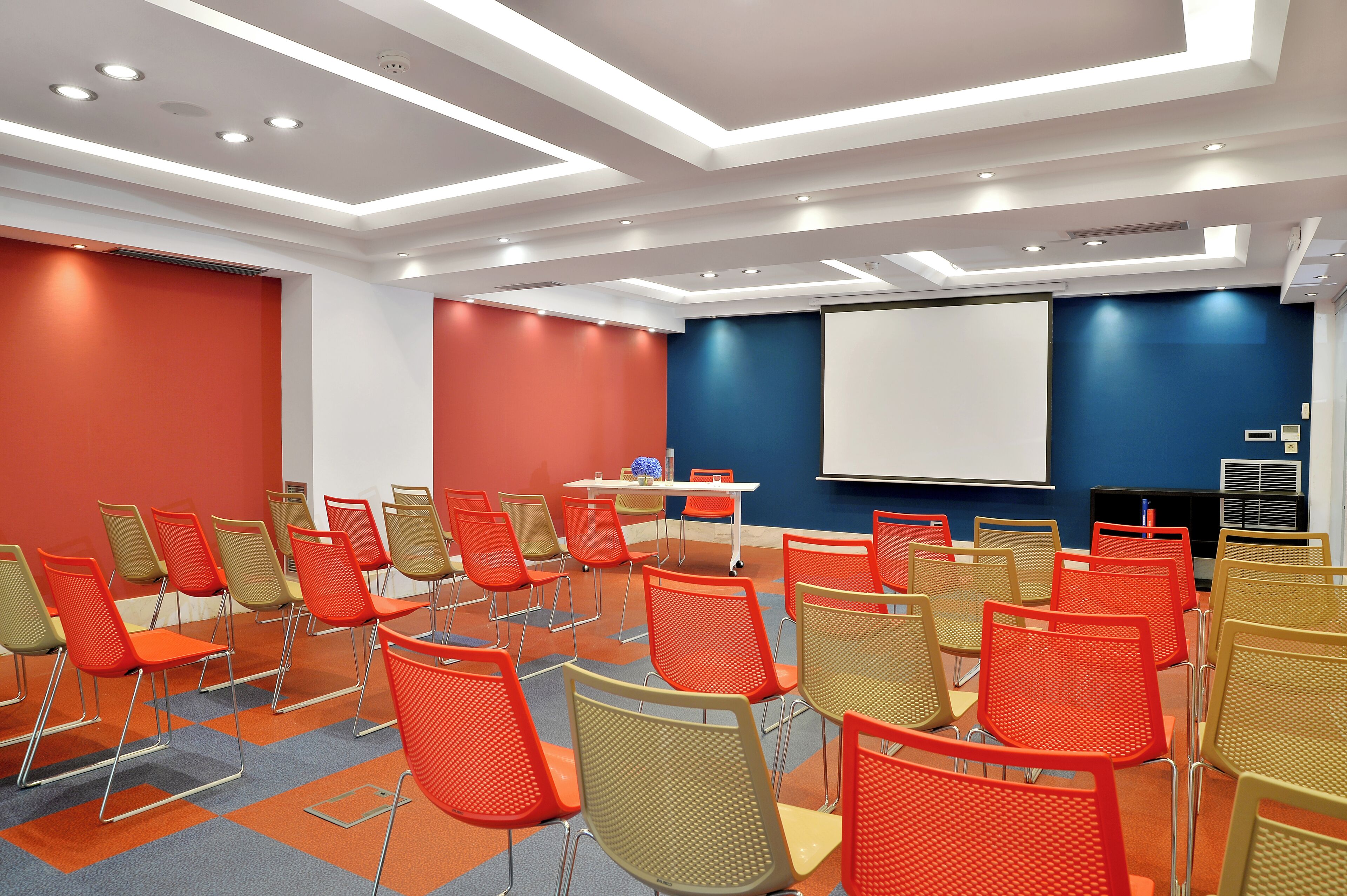 A conference room with rows of chairs, a projector screen, and a table with a laptop.