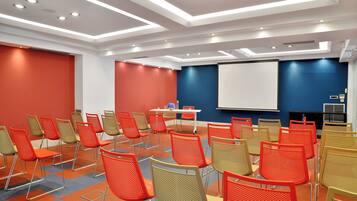 A conference room with rows of chairs, a projector screen, and a table with a laptop.