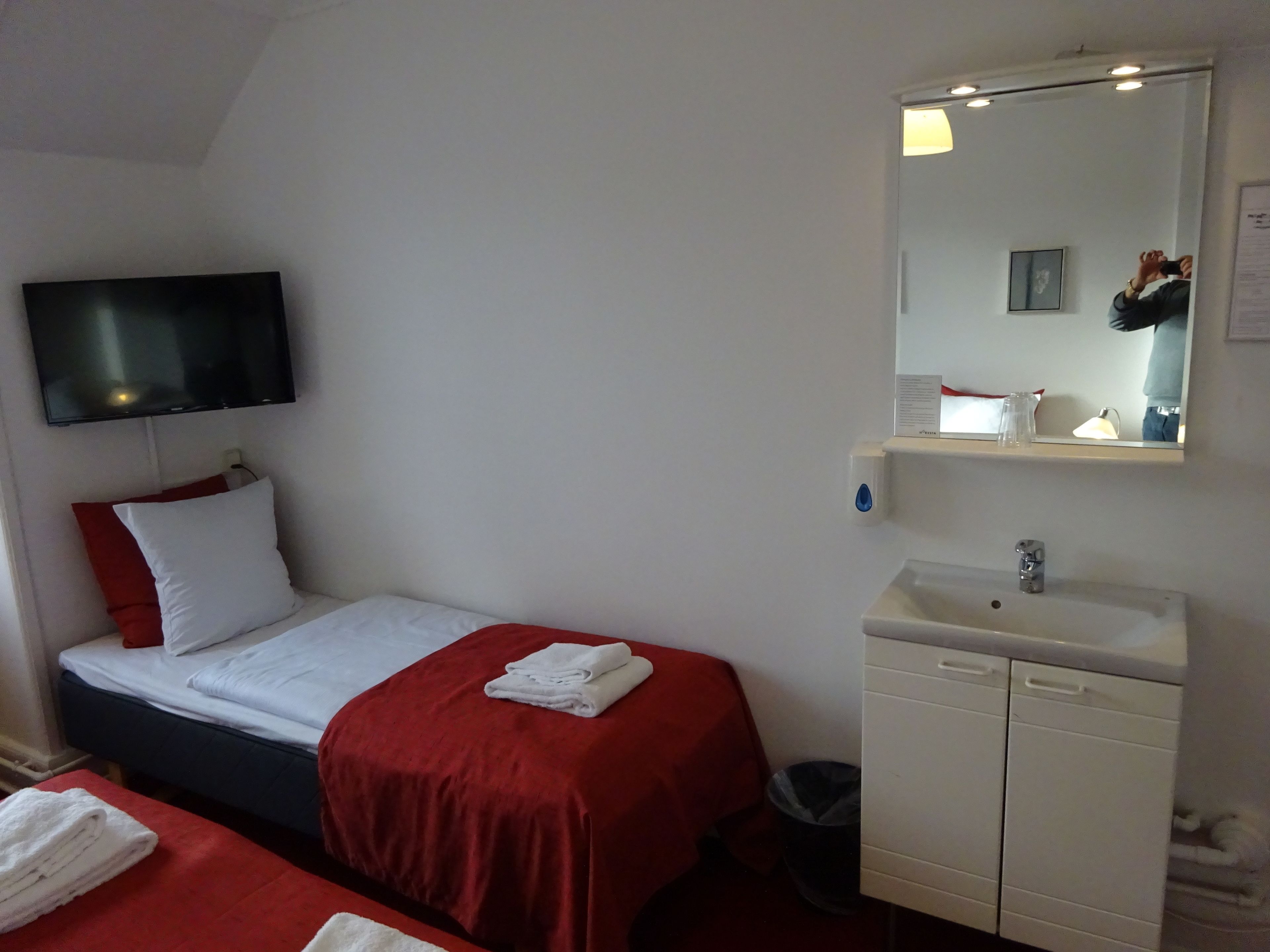 A hotel room with a bed, a TV mounted on the wall, a sink, and a mirror.