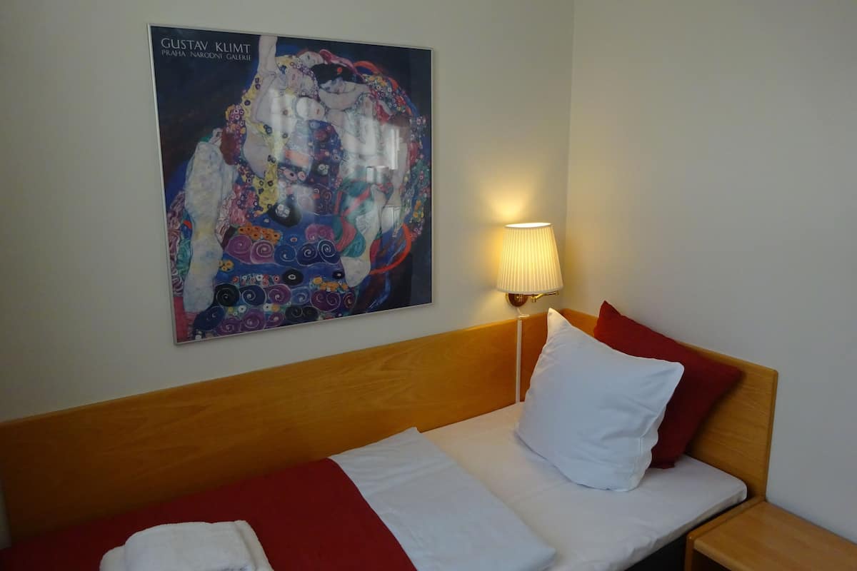 Et hotelværelse med en seng, en vægmonteret lampe og et maleri af Gustav Klimt.