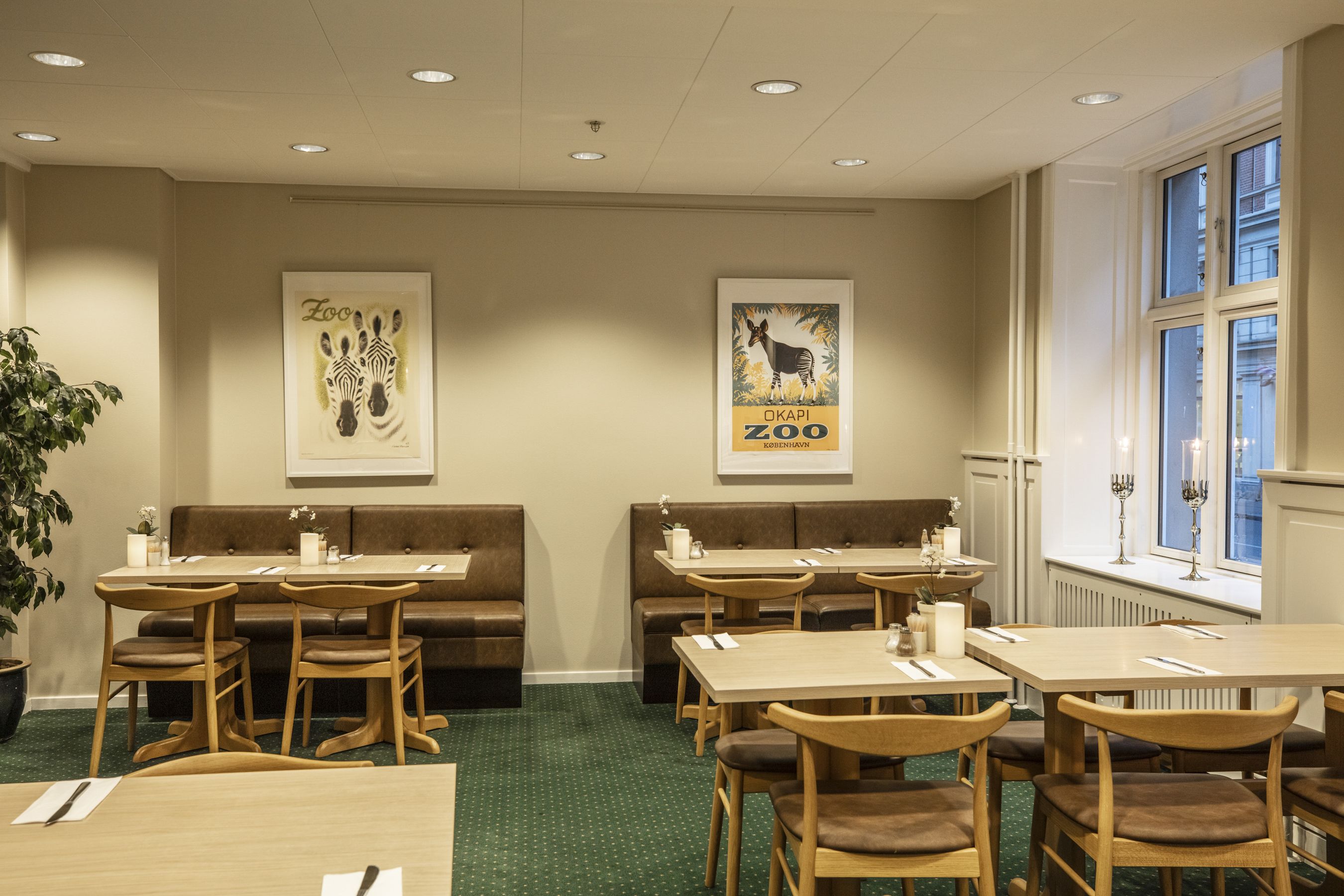 Een restaurant met zitjes en tafels, kunstwerken van een zebra en een zebra in een dierentuin, en een raam met uitzicht op de stad.