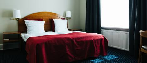 Habitación de hotel con una cama, dos lámparas de noche, una ventana con cortinas y un radiador.