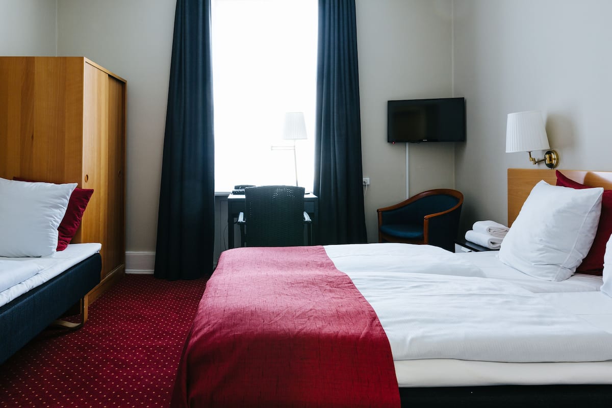Et hotelværelse med seng, skrivebord, stol, fjernsyn og garderobeskab.
