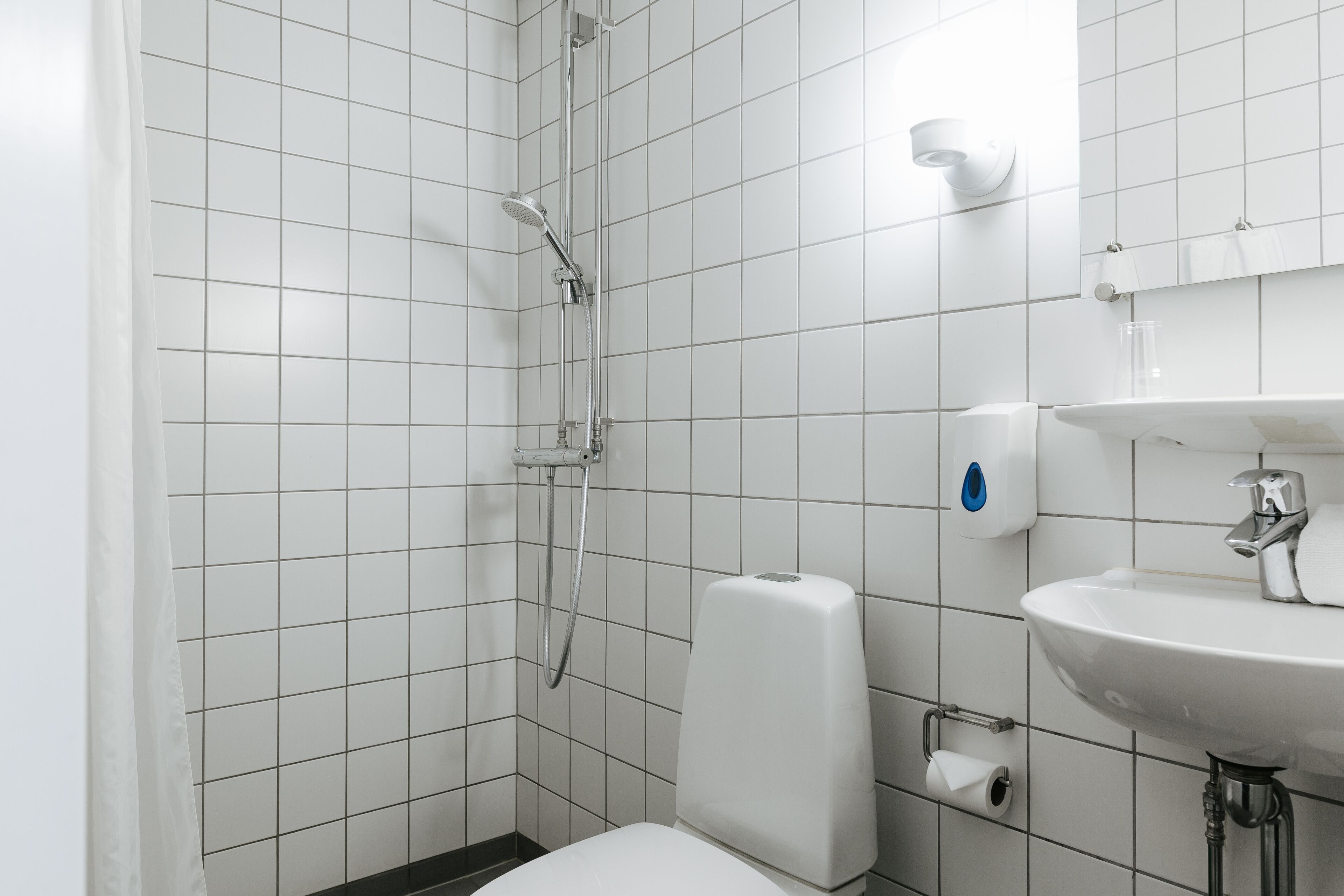 A modern bathroom with white tiles, a shower, a toilet, and a sink.