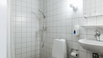Un bany modern amb rajoles blanques, dutxa, vàter i un lavabo.