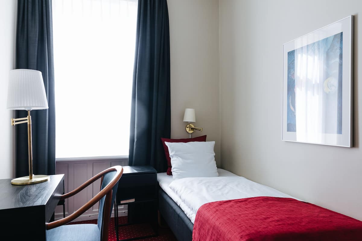 Et hotelværelse med seng, skrivebord, stol, lampe og et billede på væggen.