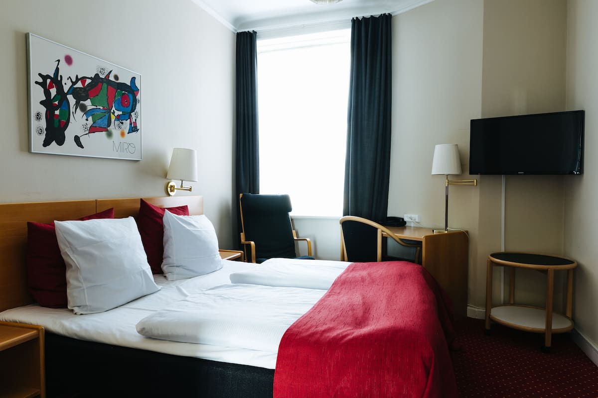 Et hotelværelse med seng, skrivebord, stol, fjernsyn og et maleri på væggen.
