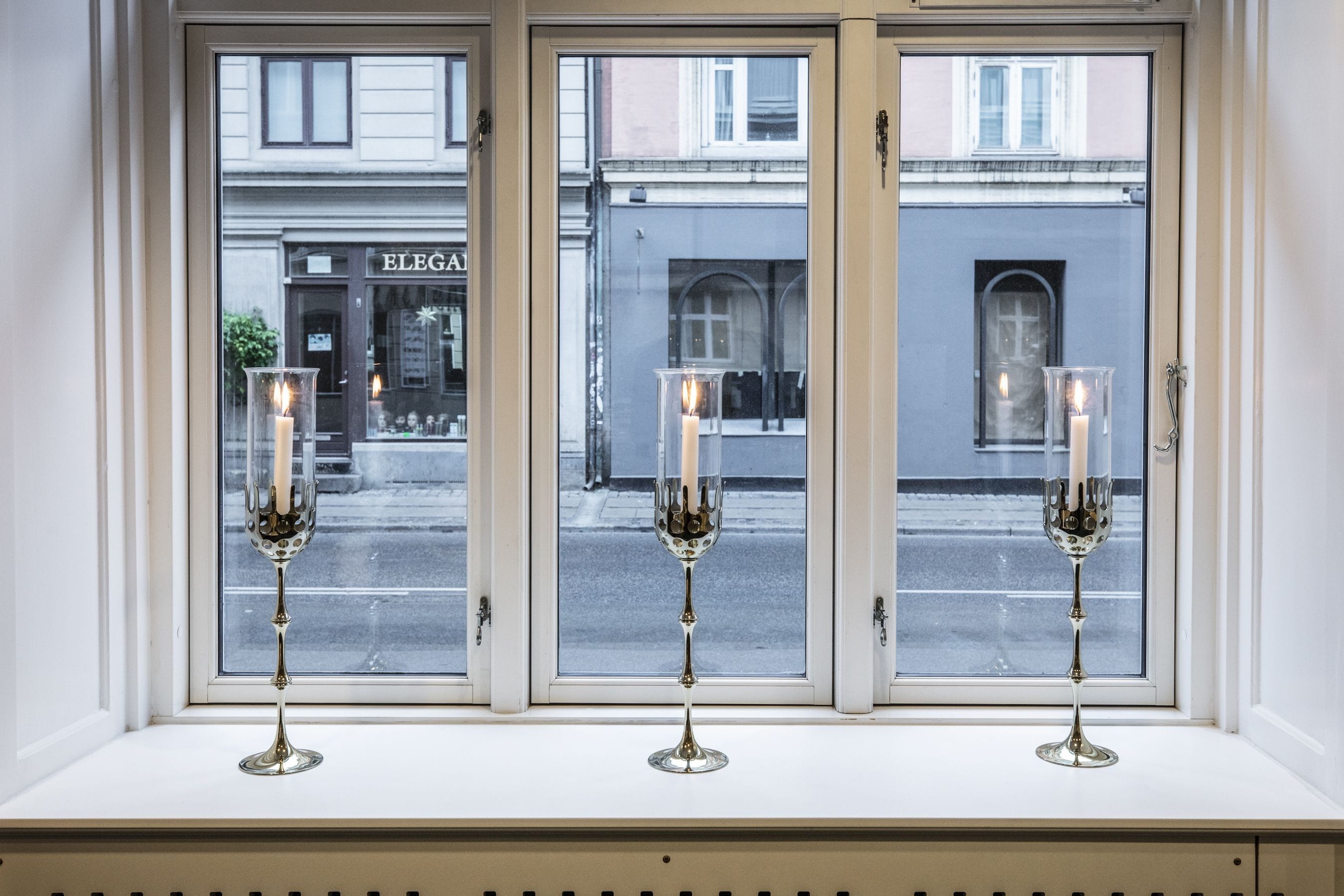 Three lit candles in glass holders on a windowsill.