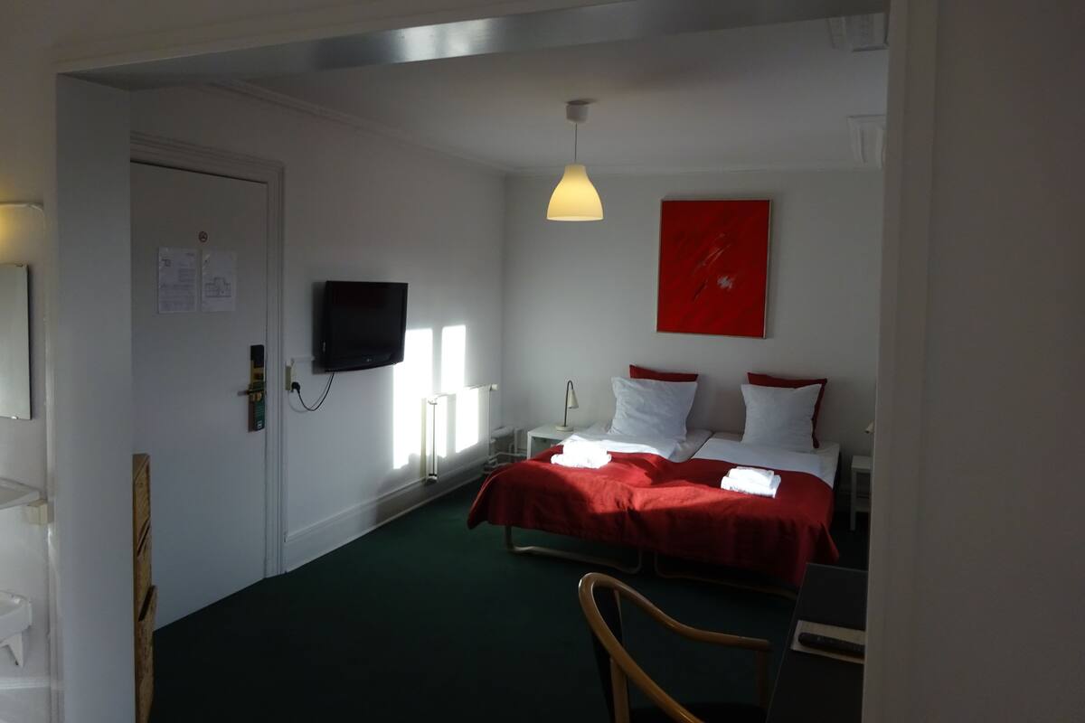 Et hotelværelse med seng, fjernsyn, et rødt kunstværk og et skrivebord.