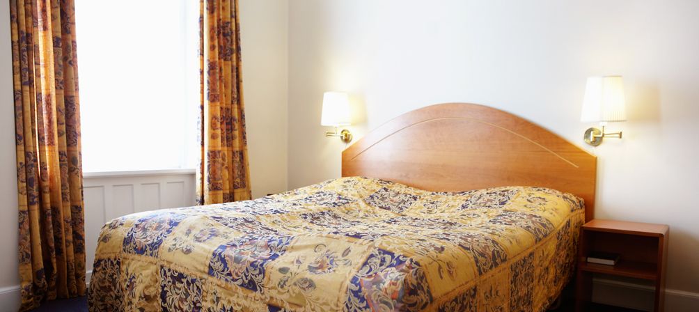 A neatly made bed with a patterned bedspread, a wooden headboard, and two bedside lamps.