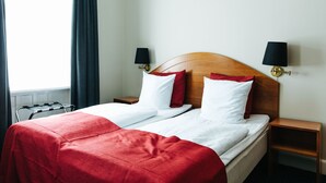 Habitación de hotel con dos camas, cabecero de madera, colcha roja, almohadas blancas y lámparas negras en mesitas de noche.