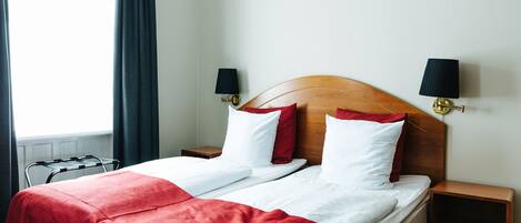 Une chambre d’hôtel avec deux lits, une tête de lit en bois, une couvre-lit rouge, des oreillers blancs et des lampes noires sur les tables de chevet.