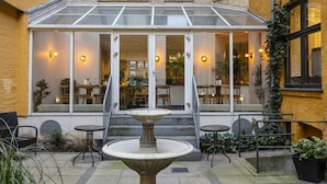 Un patio con un comedor de vidrio, una fuente central y asientos al aire libre.
