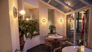 Un comedor con una mesa redonda, sillas, plantas en macetas y apliques de pared.