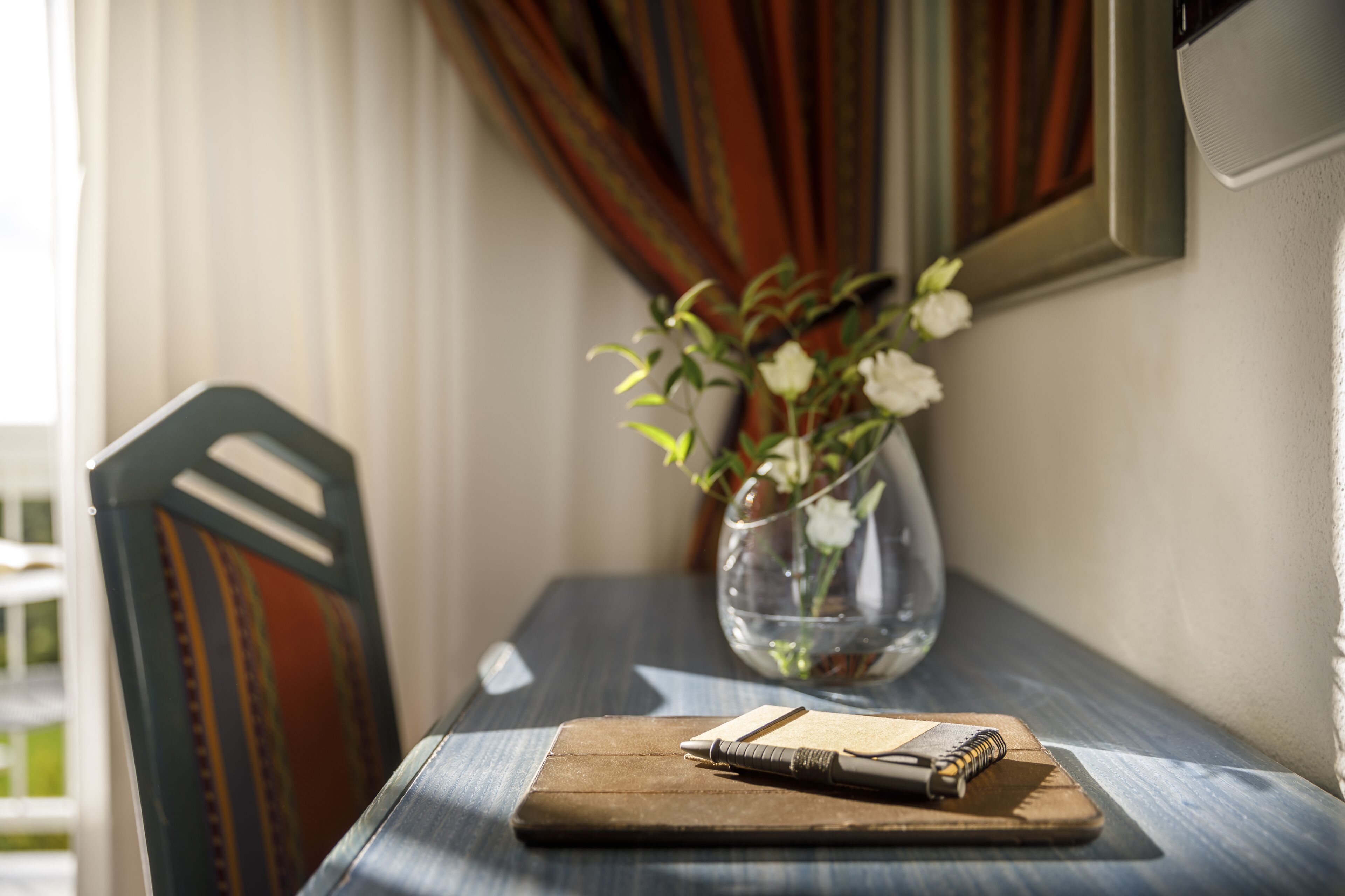 Una mesa de madera con un cuaderno, un bolígrafo y un florero con flores.