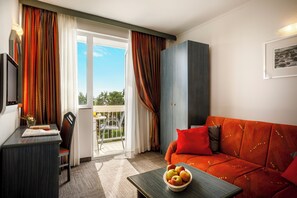 Une pièce comprenant un canapé, un bureau, une chaise, une table avec des fruits, et donnant sur l’extérieur grâce à une porte vitrée.