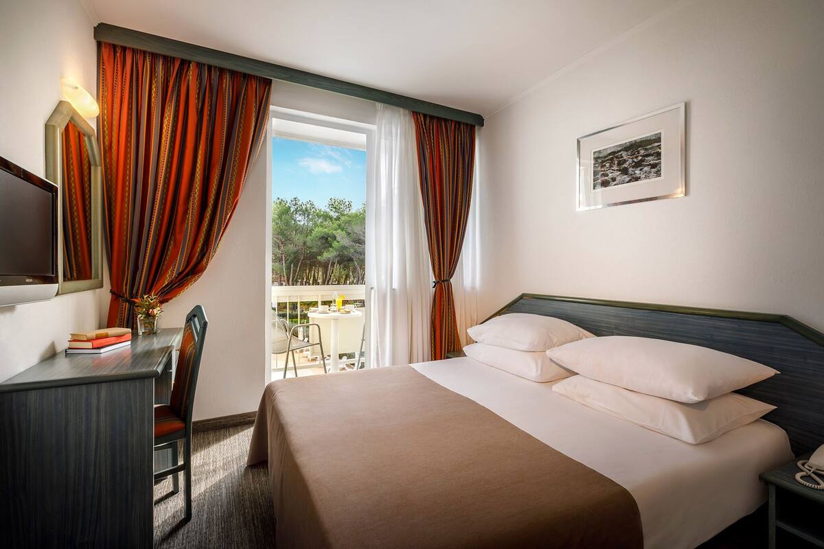 Habitación de hotel con cama, escritorio, silla, teléfono y ventana con cortinas.