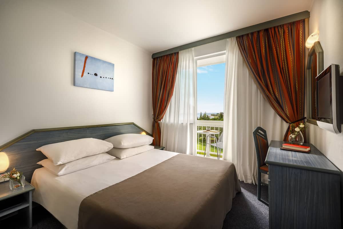 Una habitación de hotel con una cama grande, un escritorio con una silla, un televisor y un balcón con cortinas.