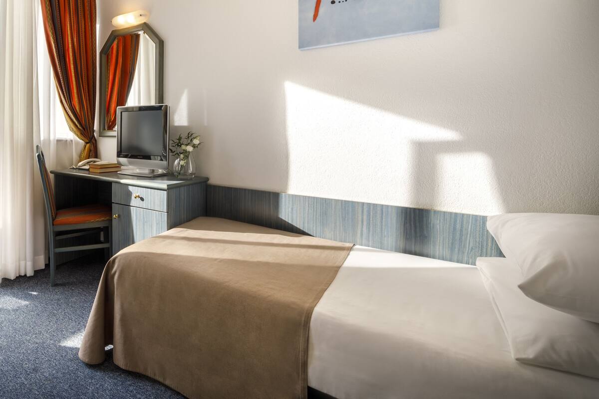 Una habitación de hotel con cama, escritorio con computadora, una silla y un cuadro en la pared.