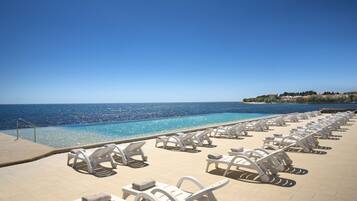 A poolside area with white lounge chairs and a clear view of the ocean.