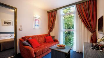 Ein Hotelzimmer mit einer roten Couch, einem kleinen Tisch mit Obst, einem Bett und einem Fenster mit Vorhängen.