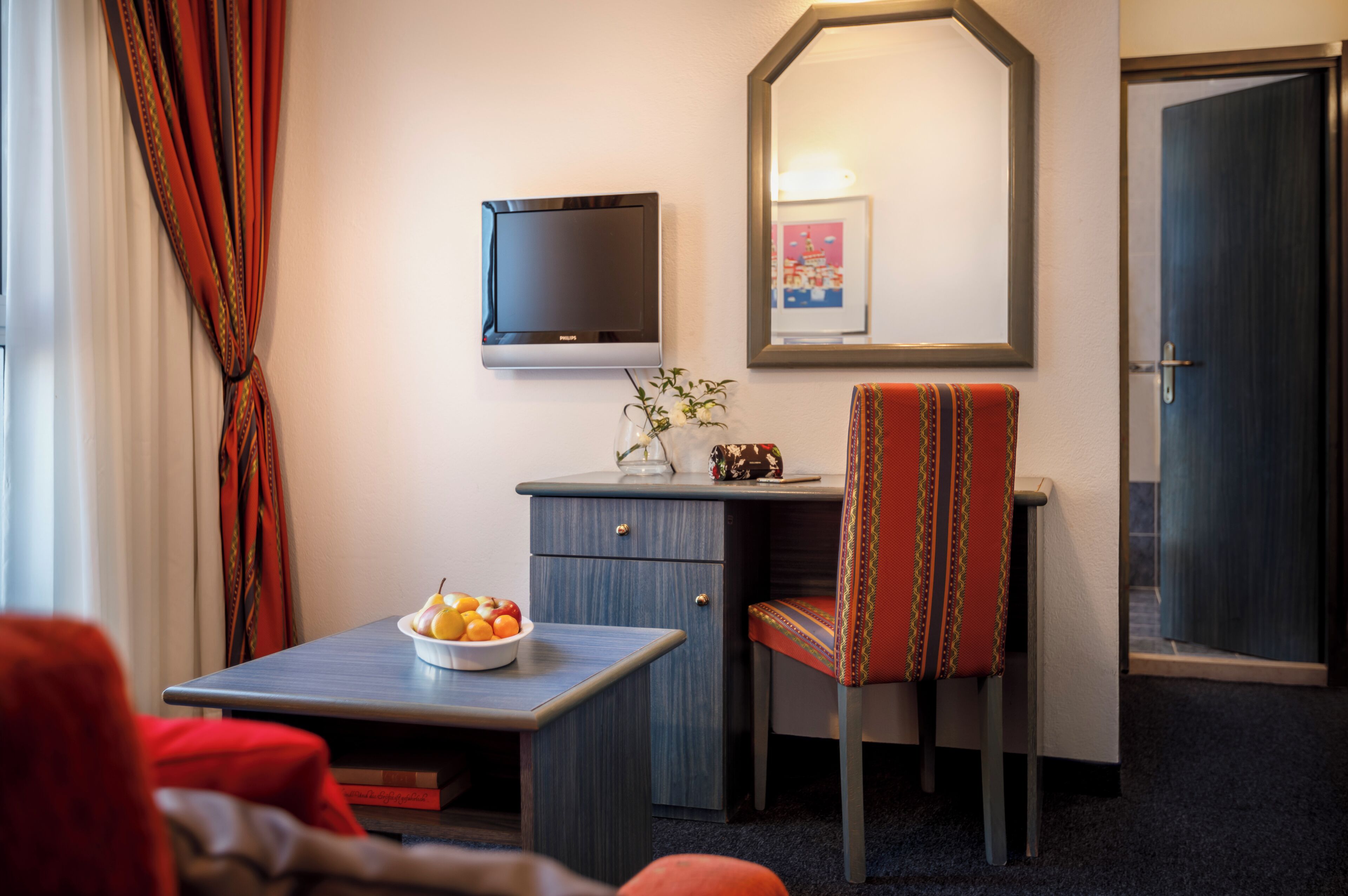 Habitación de hotel con escritorio, silla, televisor y un cuadro en la pared.
