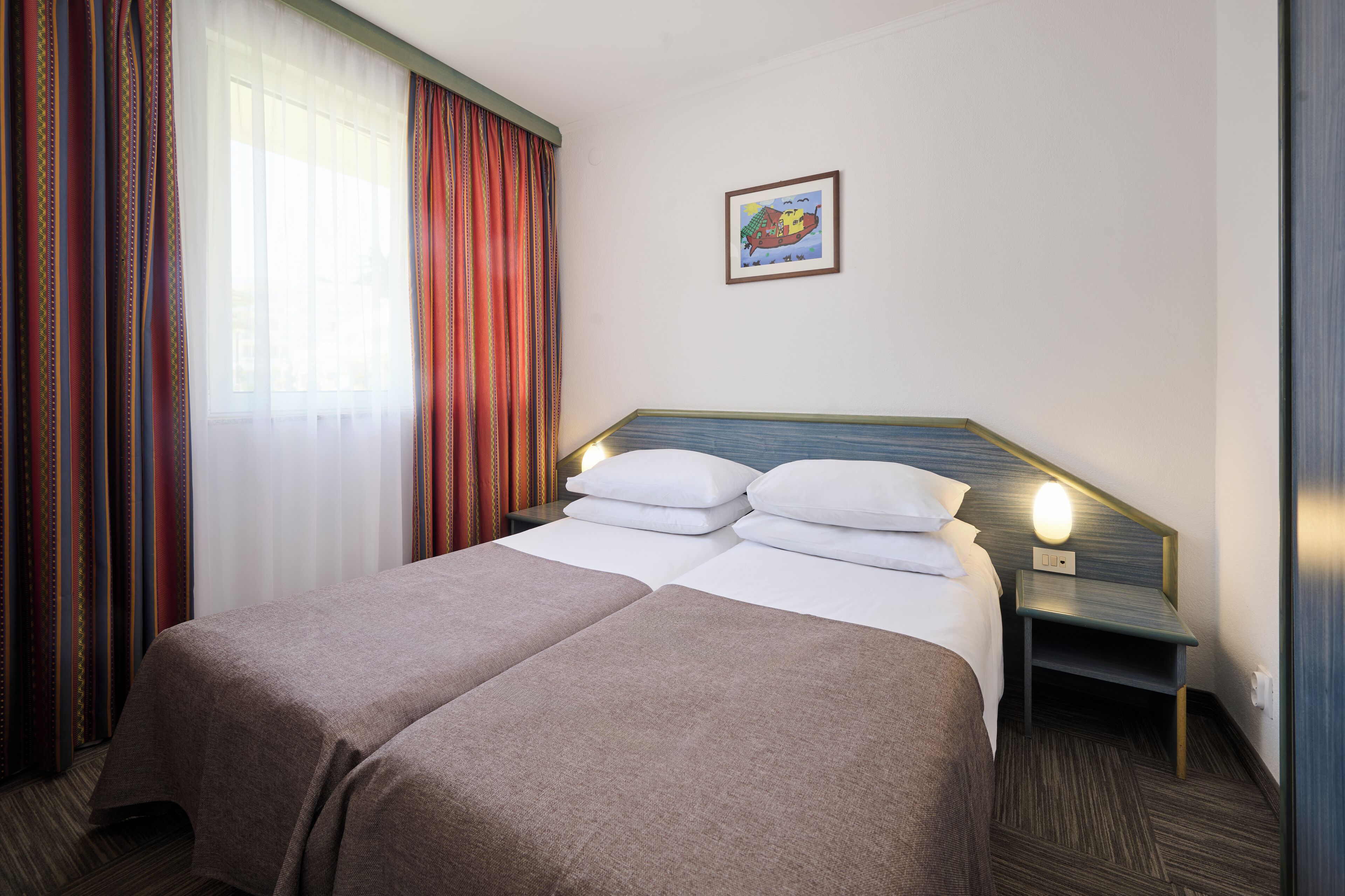Een hotelkamer met twee bedden, een nachtkastje, een wandlamp en een raam met gordijnen.