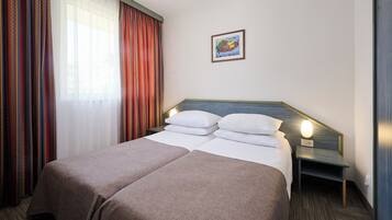 Een hotelkamer met twee bedden, een nachtkastje, een wandlamp en een raam met gordijnen.
