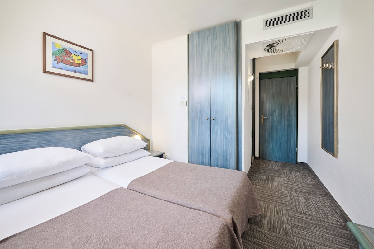 Habitación de hotel con dos camas, un armario grande, un cuadro en la pared y un pasillo que conduce a otra habitación.