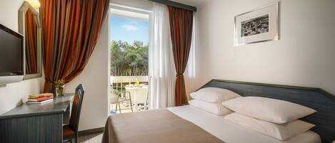 Una habitación de hotel con cama, escritorio, silla, teléfono y ventana con cortinas.
