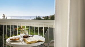 A table with a book, a glass of drink, and a plate with food on a balcony overlooking a scenic view. - Laguna Maradiso Hotel by Aminess  (Novigrad)