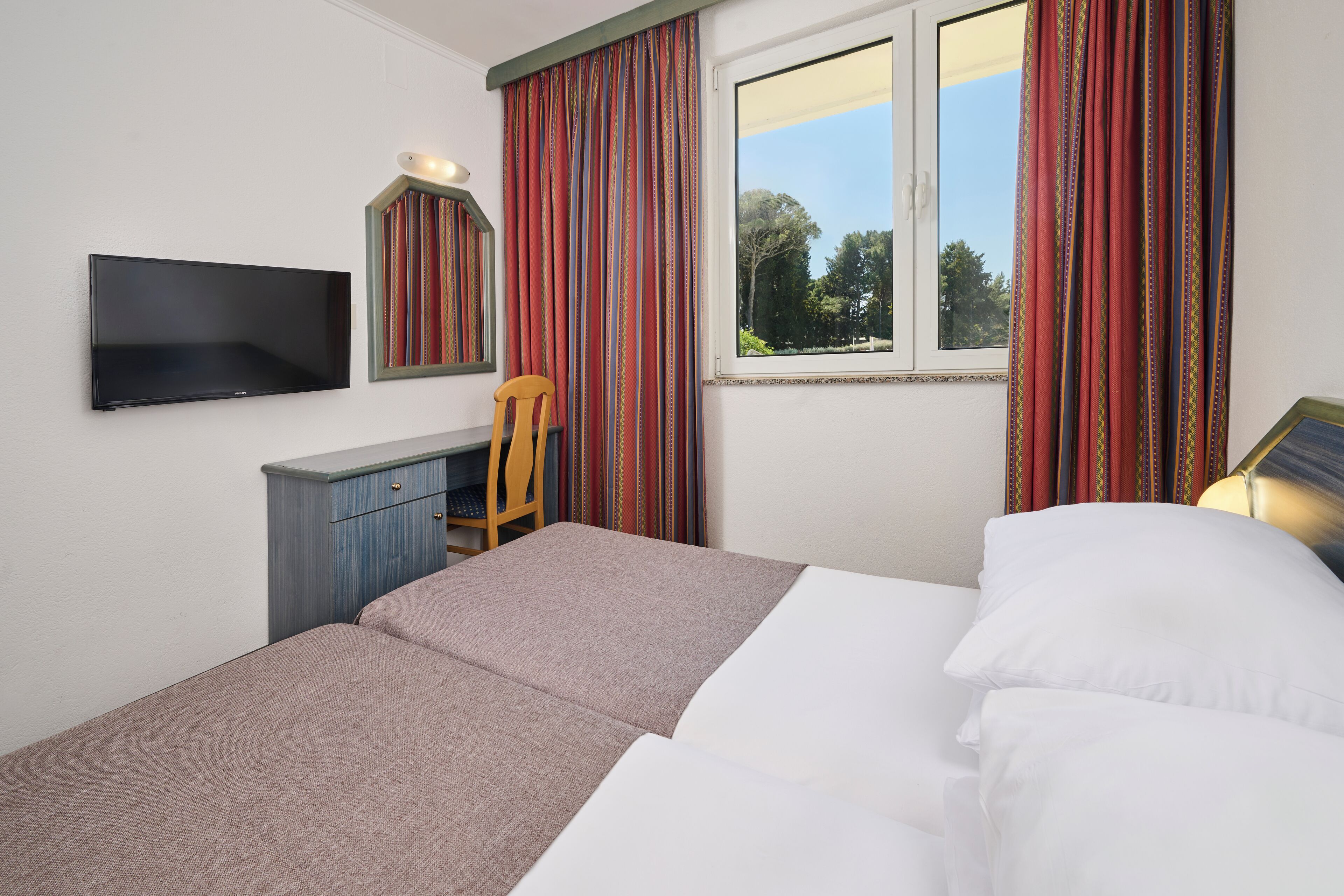 Hotelkamer met een bed, bureau met stoel, televisie aan de muur en raam met gordijnen.