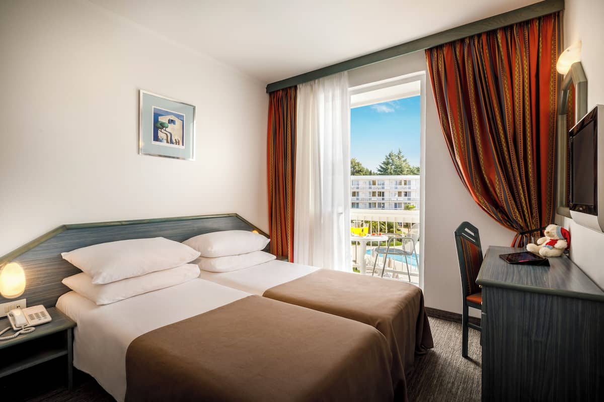Habitación de hotel con dos camas, un escritorio, una silla, teléfono, un cuadro en la pared y vistas al exterior.
