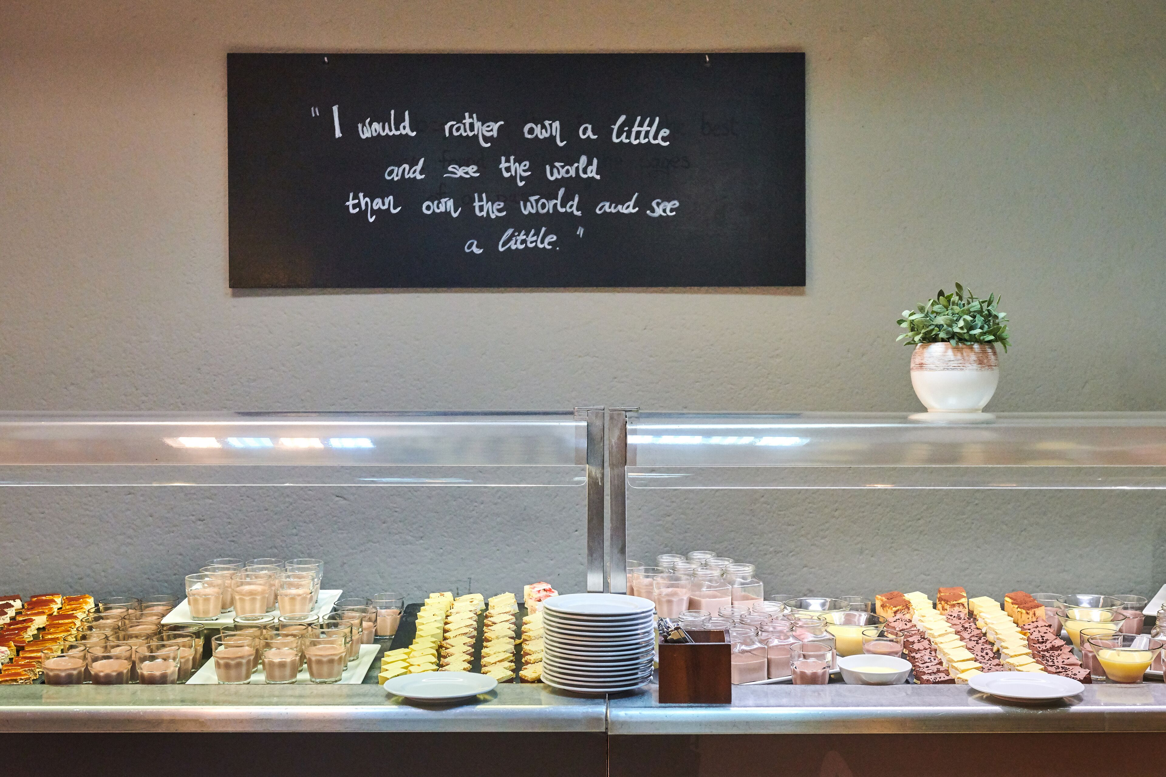 Ein reichhaltiges Buffet mit verschiedenen Desserts und Getränken, eine Tafel mit einem Zitat und ein Blumentopf.