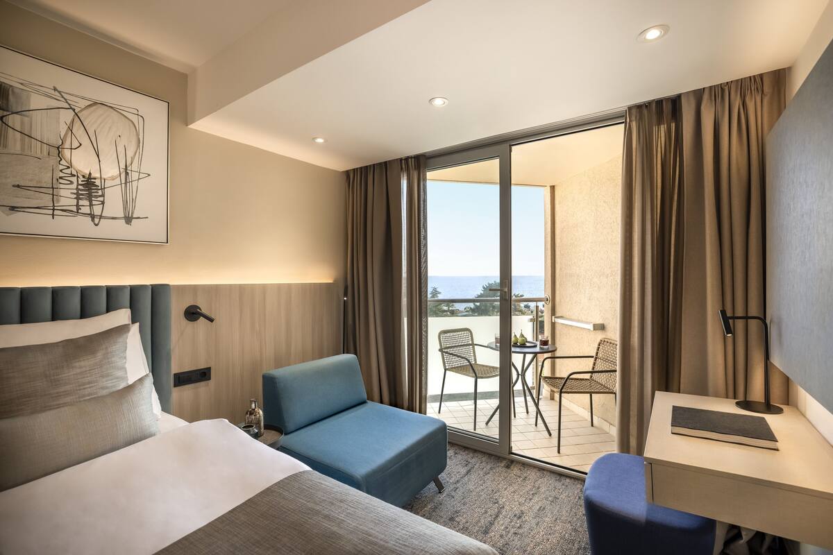A hotel room with a bed, a desk, a chair, and a balcony with a table and chairs.