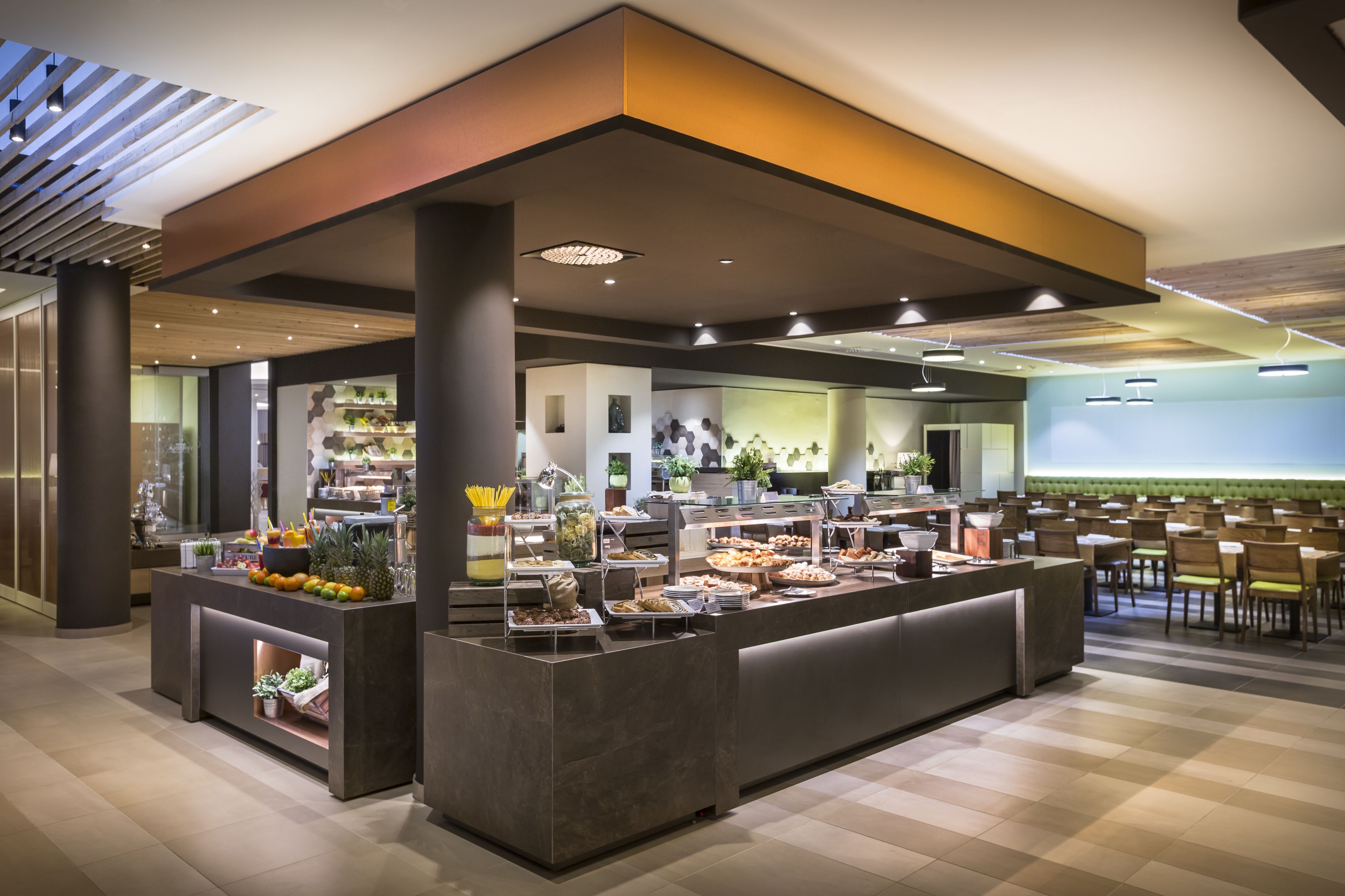 A buffet area with various food stations, a seating area with chairs, and a counter with a display of fruits and vegetables.