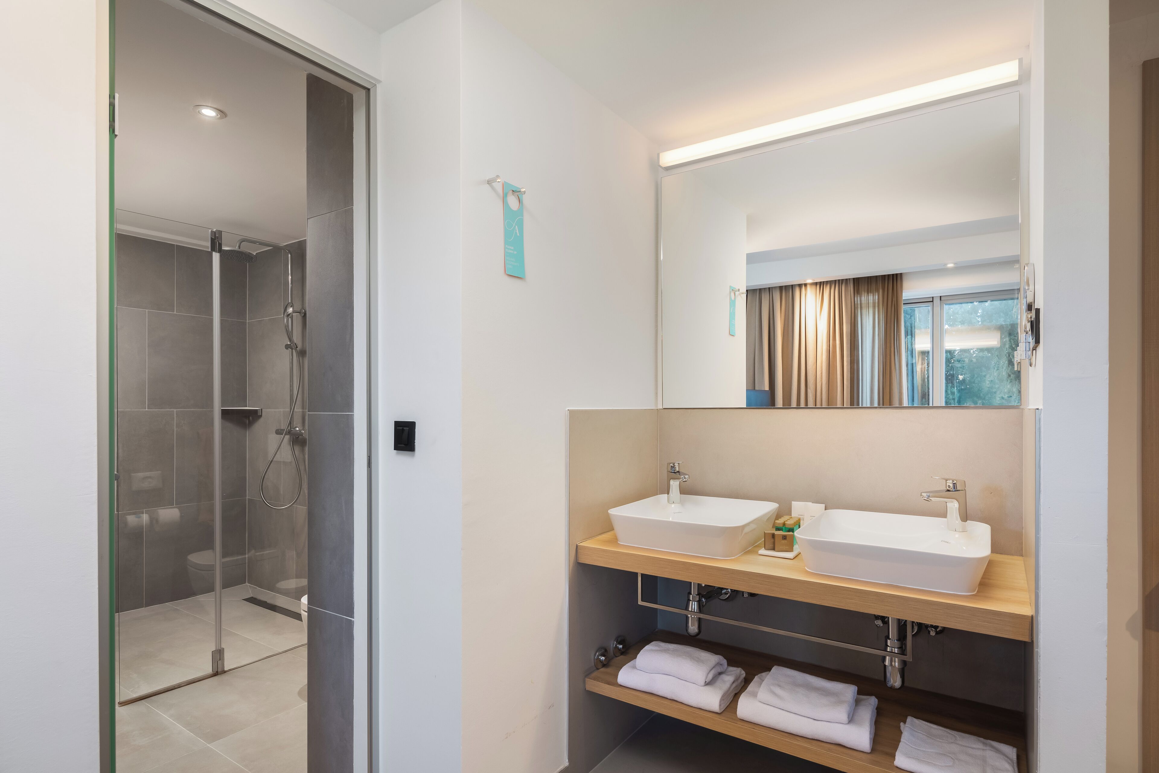 Een moderne badkamer met een douche met glazen wand, twee wasbakken en een spiegel boven het badmeubilair.