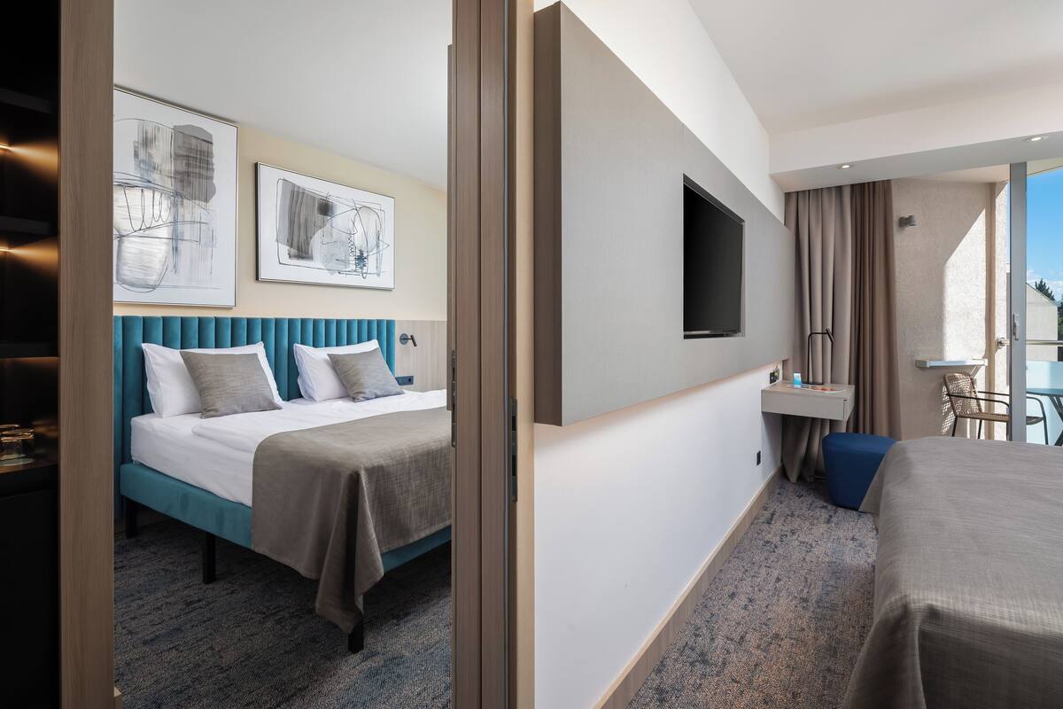 A hotel room with a bed, a desk, a TV, and artwork on the wall.