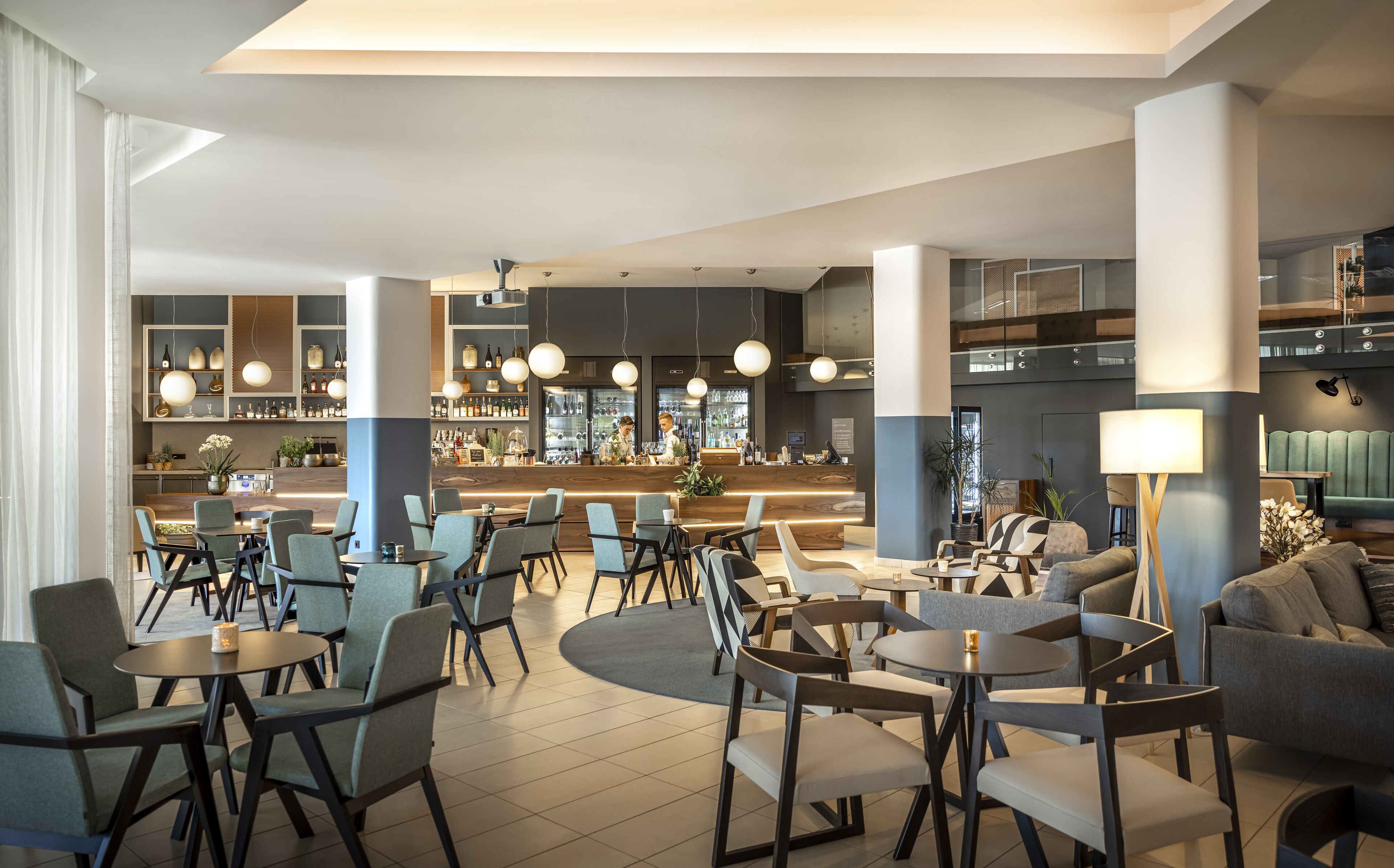 Un moderno vestíbulo de hotel con zona de bar, espacios de descanso y una mezcla de decoración contemporánea y clásica.
