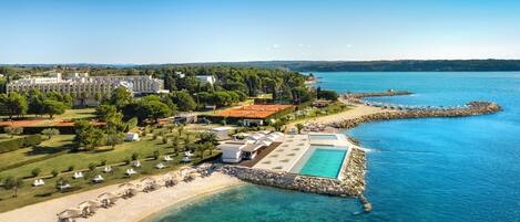 Oversigtsbillede af et kystresort med swimmingpool, strand og et stort kompleks af bygninger.