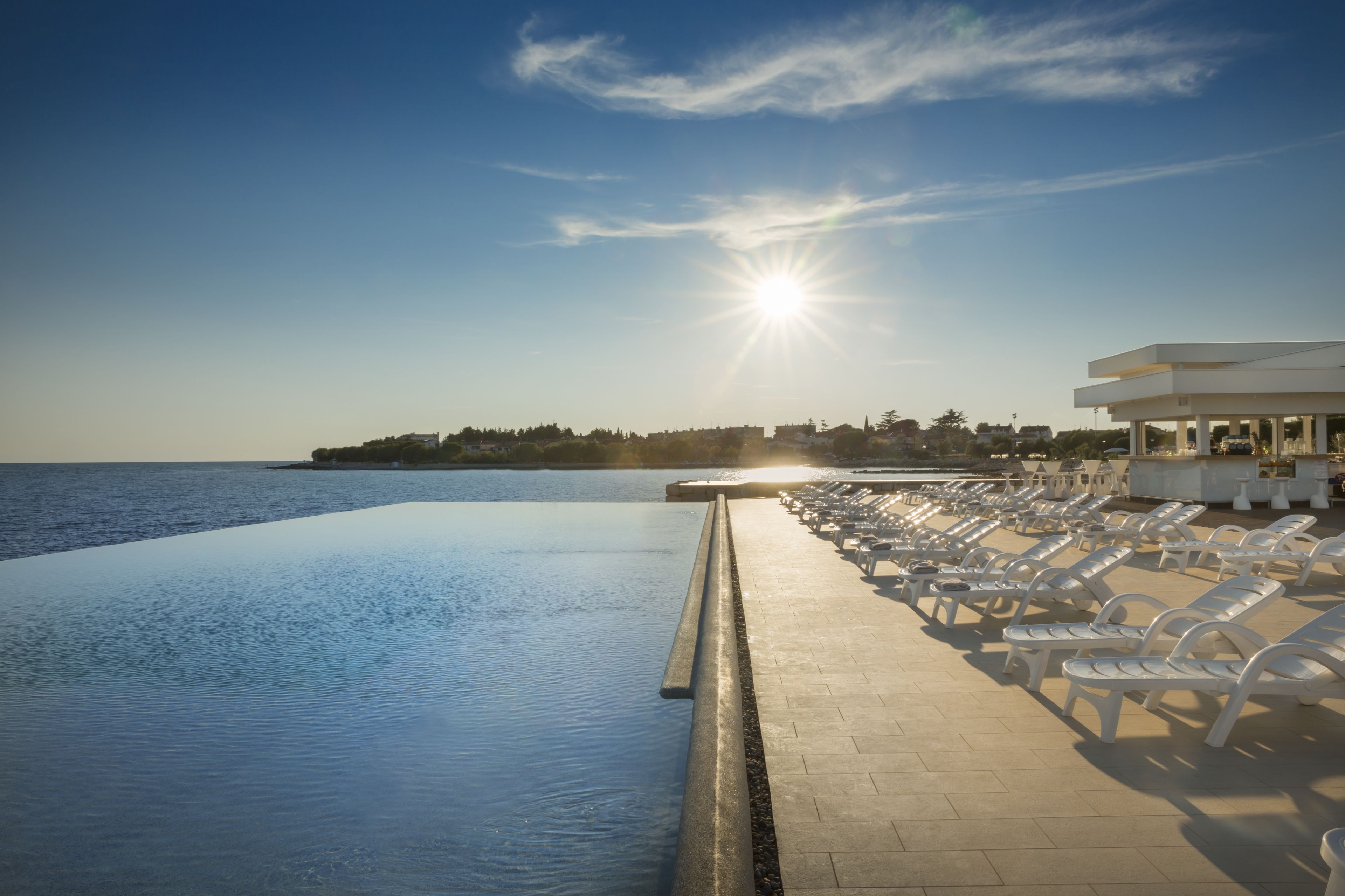 Una piscina infinita con vista al mar y una fila de sillones blancos.