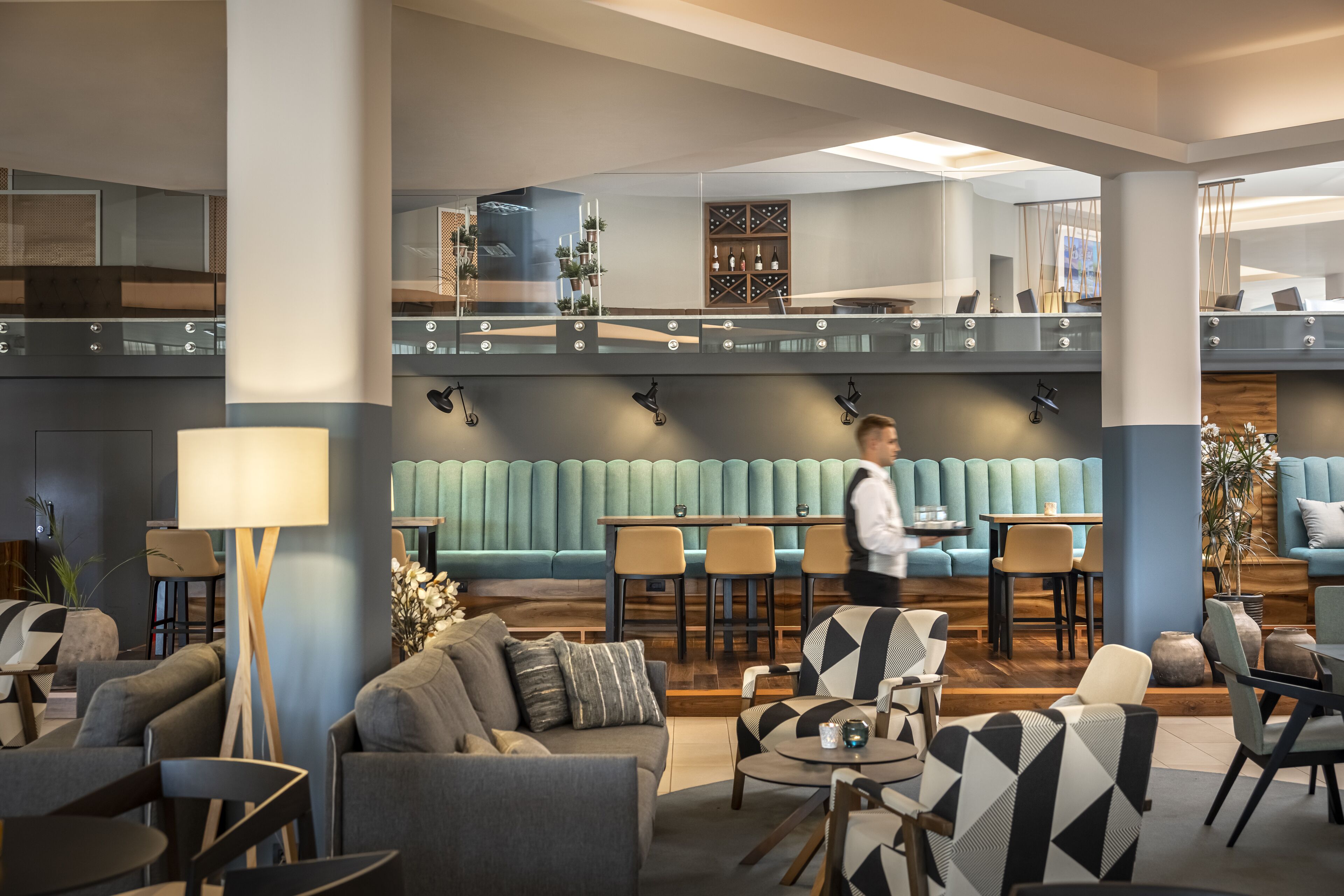 A modern hotel lobby with a seating area, a staircase, and a bar.