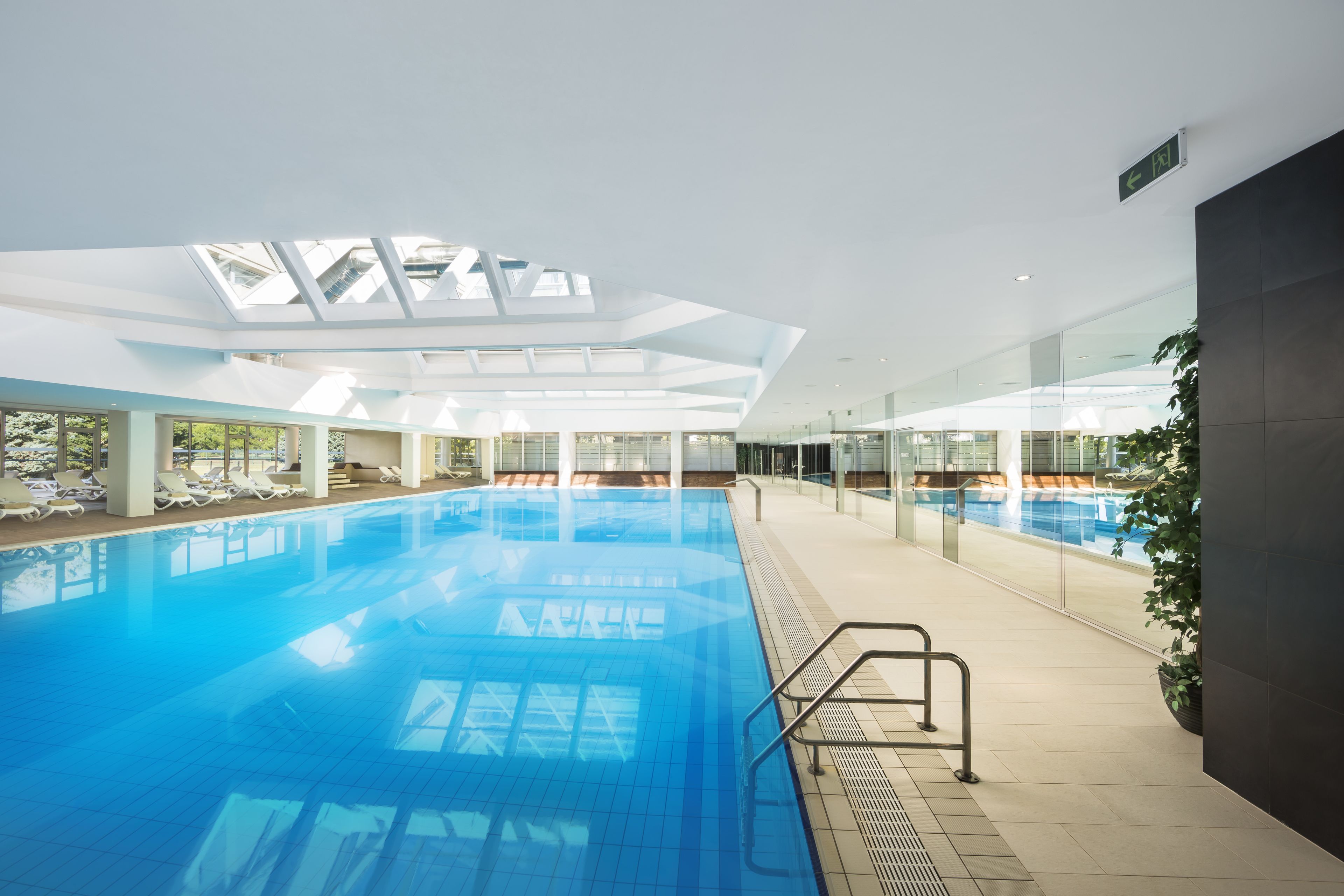 Una piscina interior con paredes de vidrio transparente, tragaluces y suelo de baldosas.