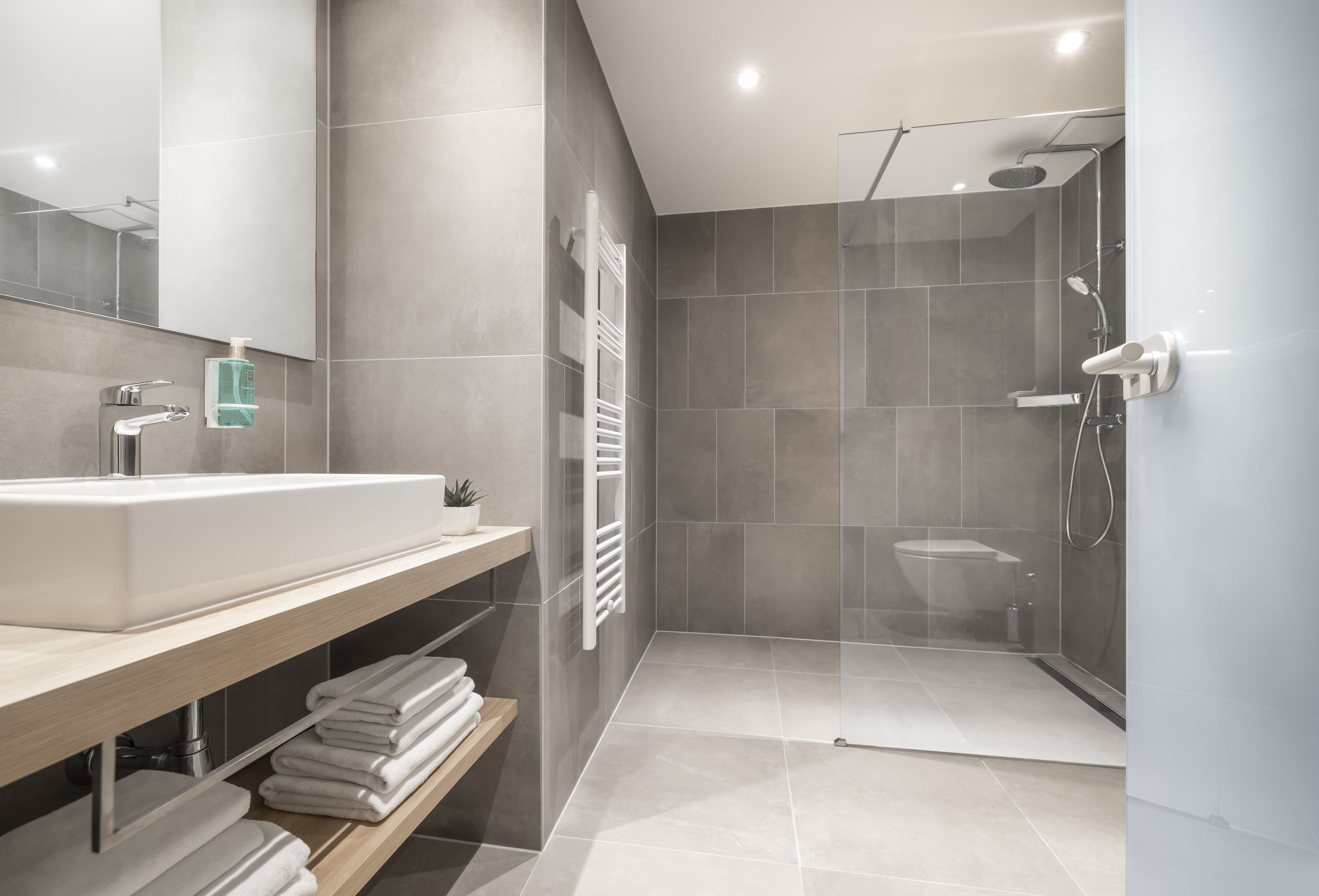 A modern bathroom with a large sink, mirror, towel rack, and a glass-enclosed shower area.