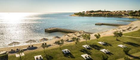 An aerial view of a coastal resort with a beach, lounge chairs, and a pool area.