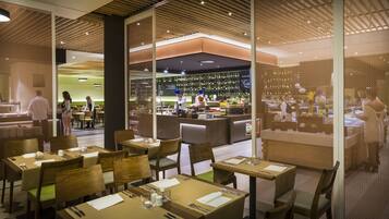 A restaurant with wooden furniture, a bar area, and a view of the dining area through a glass partition.