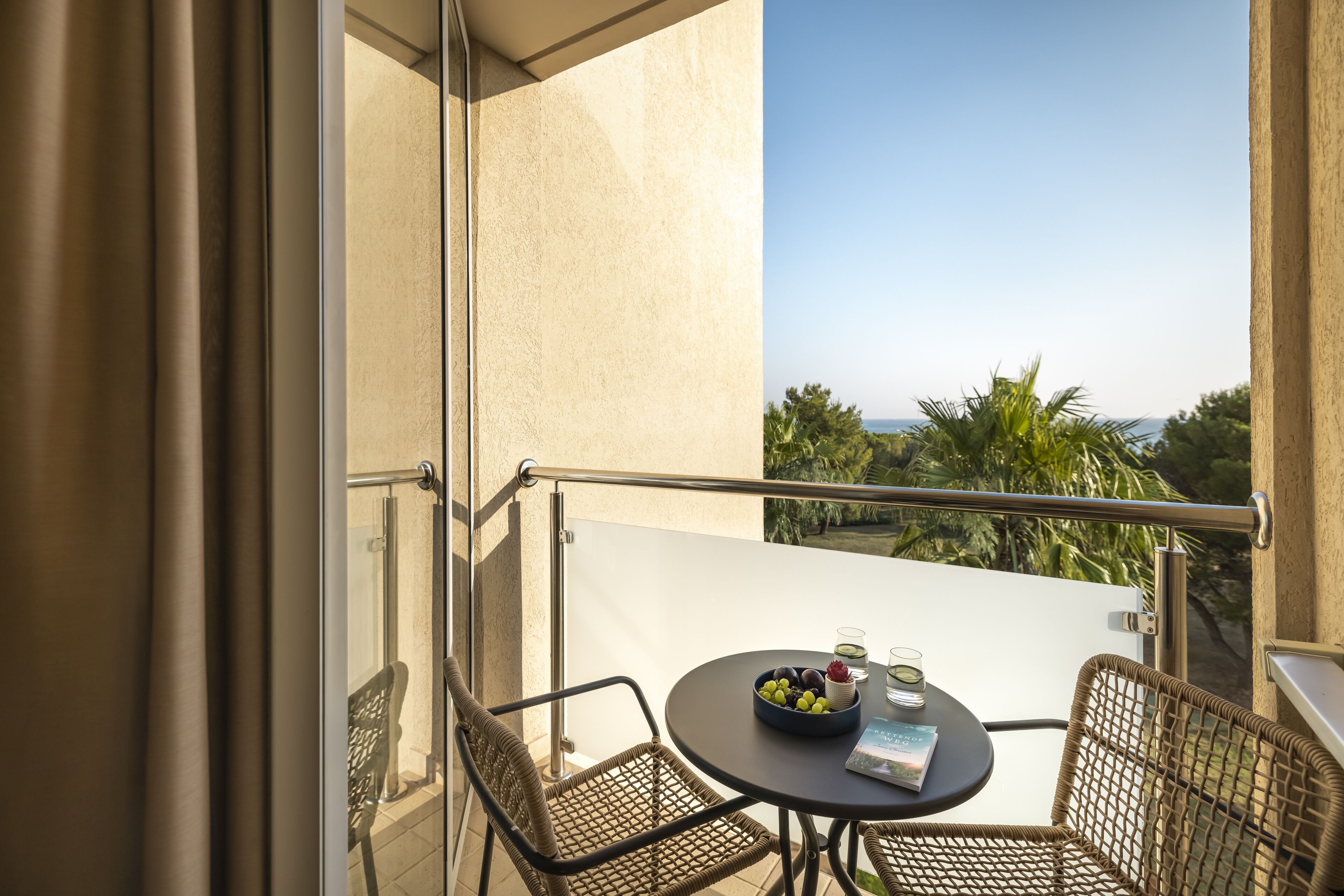 A balcony with wicker chairs, a small round table, and a bowl of fruit.