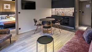 A modern living room with a round table, two chairs, a sofa, and a kitchen area with a sink and stove. - Hotel Restaurant & Spa Verte Vallée (Munster)