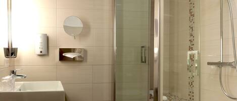 A modern bathroom with a glass-enclosed shower, a sink with a mirror, and a soap dispenser on the wall.